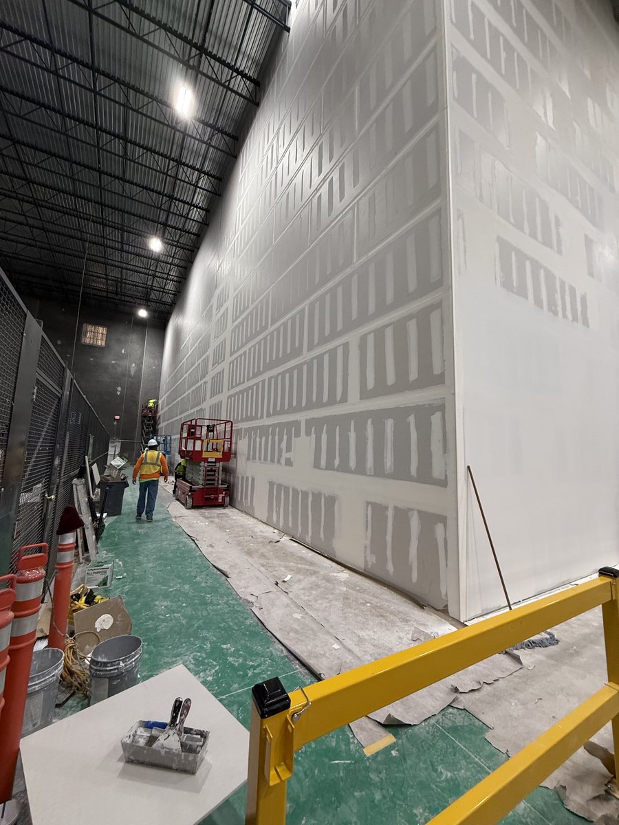 Two-story drywall wall under finish with crew on a scissor lift
